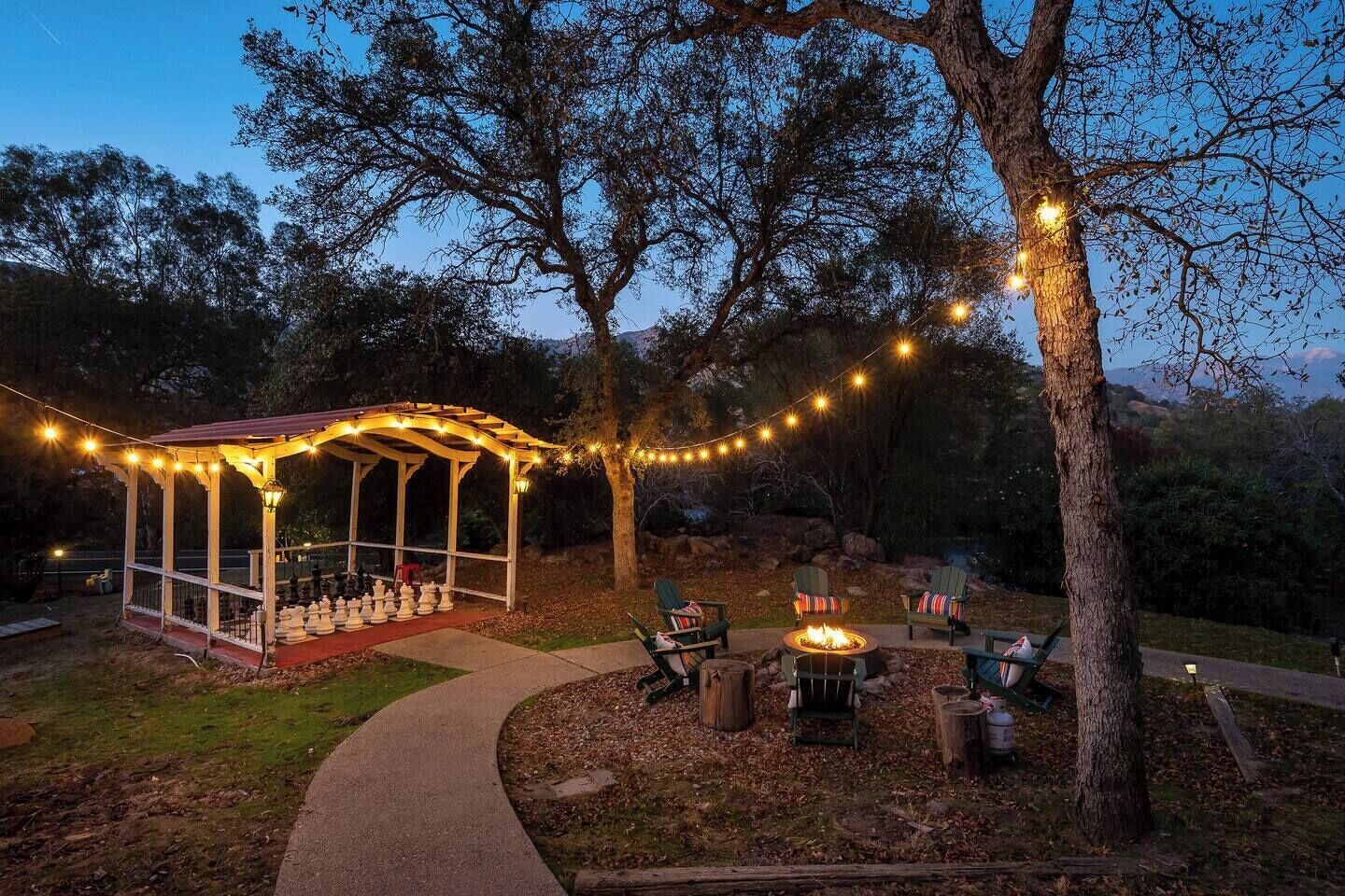 A gazebo with string lights, outdoor seating, and a fire pit.