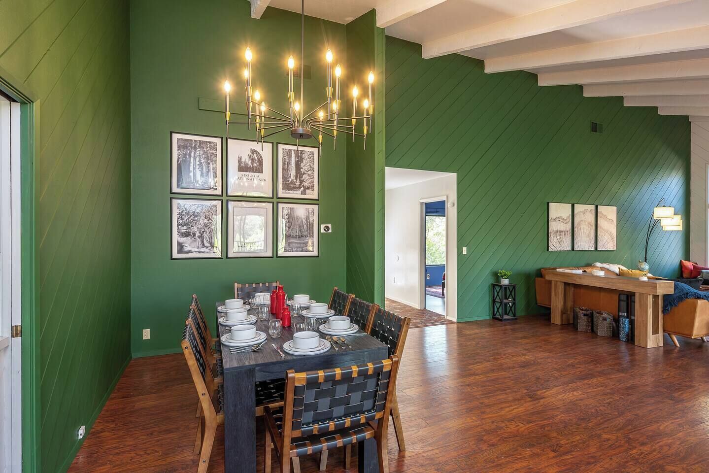 A dining area with a table set for six, a chandelier, and framed pictures on the wall.
