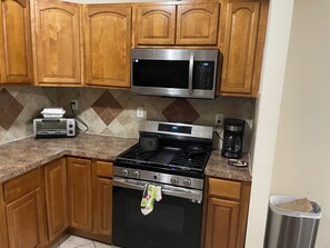 A kitchen with wooden cabinets, a stainless steel microwave, a toaster, a stove, and a coffee maker. - 6-bedroom apartment in terrific Jersey City with AC (Jersey City)