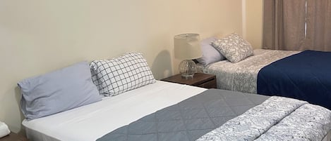 Quarto com duas camas, uma mesa de cabeceira, abajur e janela com cortinas.