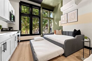 A modern bedroom with a bed, bedside tables, and a view of trees through large windows. - Stay Central Near Petco Park & Gaslamp (San Diego)
