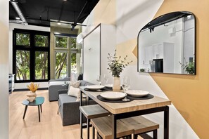 Un comedor moderno con una mesa de madera dispuesta para dos personas, un sofá y vistas al exterior a través de amplios ventanales.