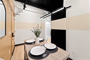 A dining area with a wooden table set for two, a vase with a plant, and a black wall with a sliding door. - Stay Central Near Petco Park & Gaslamp (San Diego)