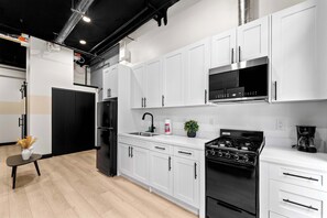 A modern kitchen with white cabinets, a black refrigerator, a stainless steel microwave, a gas stove, and a coffee maker. - Stay Central Near Petco Park & Gaslamp (San Diego)