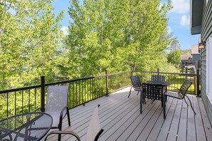 A wooden deck with metal chairs and a table, surrounded by trees.