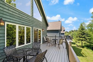 A wooden deck with outdoor furniture, large windows, and a view of the surrounding greenery.
