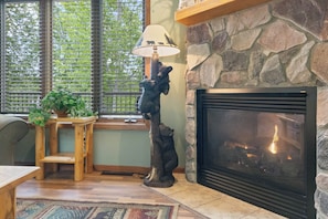 A fireplace with a stone surround, a bear statue, a lamp with a bear design, and a window with blinds.