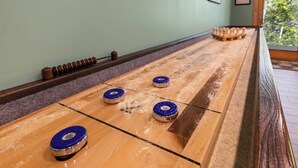 Uma mesa de shuffleboard com quatro discos, piso de madeira e janela com vista para árvores.