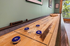 A shuffleboard table with four pucks, a wooden floor, and a window with a view of trees. - Giants Ridge lakefront Villa 4bdrm with gameroom (Biwabik)