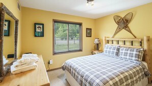 Um quarto com uma cama, uma janela com persianas, uma mesa de cabeceira com abajur e um espelho na parede.
