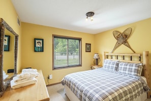 A bedroom with a bed, a window with blinds, a bedside table with a lamp, and a mirror on the wall. - Giants Ridge lakefront Villa 4bdrm with gameroom (Biwabik)