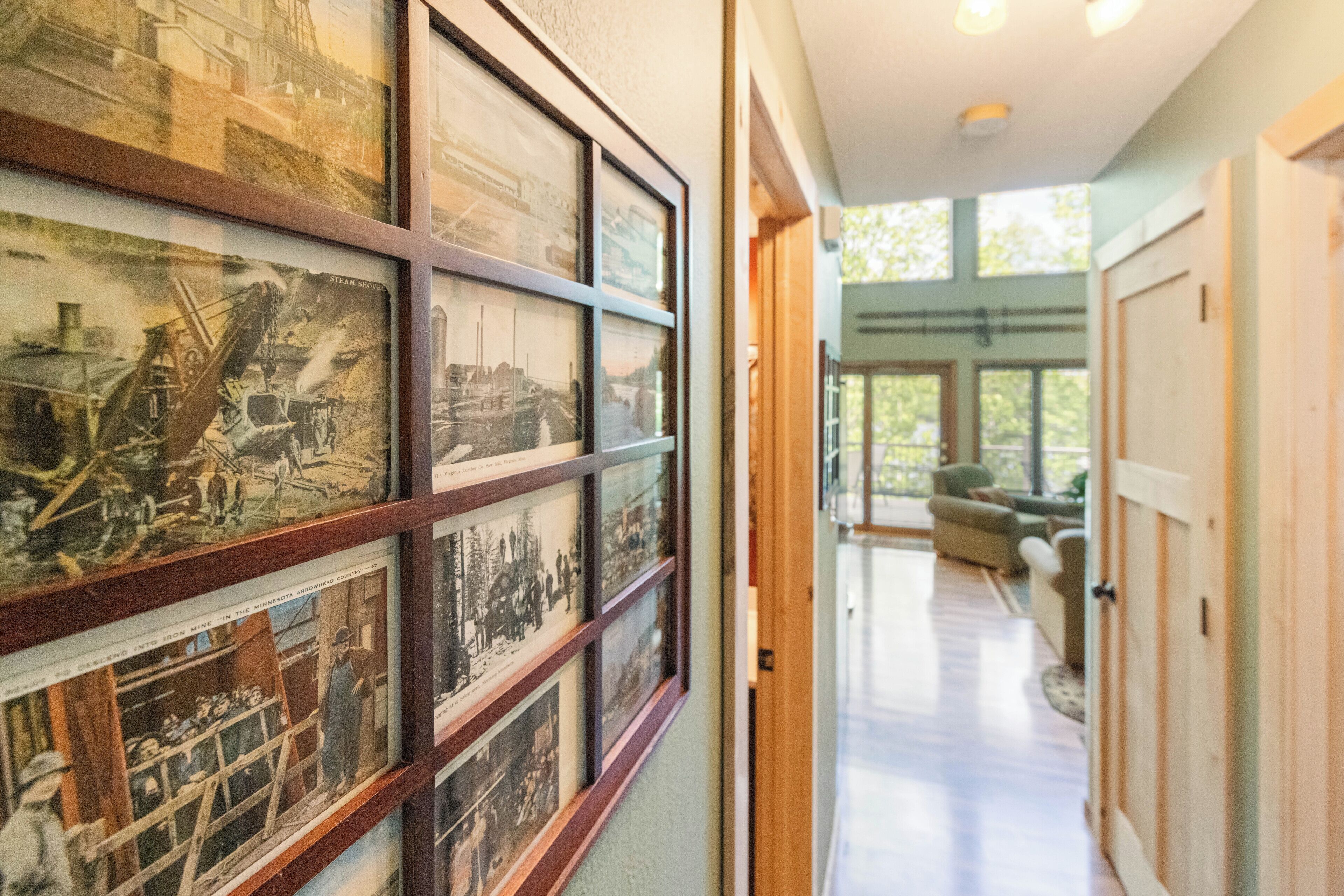A hallway with framed historical photographs on the wall, a wooden door, and a view into a room with a large window.