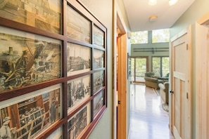 A hallway with framed historical photographs on the wall, a wooden door, and a view into a room with a large window.
