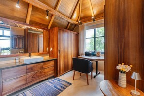 Ein modernes Badezimmer mit Holzsärchen, einem großen Spiegel, einem Waschbecken und einem Fenster mit Tageslicht.
