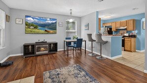 Una sala de estar moderna con chimenea, un comedor con sillas azules y una cocina con muebles de madera.