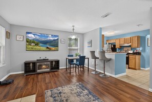 Ein modernes Wohnzimmer mit Kamin, einem Essbereich mit blauen Stühlen und einer Küche mit Holzausstattung.