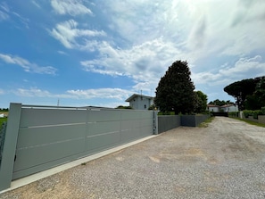 A gated driveway leading to a residential area with a large tree and houses in the background. - Villa with garden and free parking—25min from Venice—3 bedrooms,2 bathrooms, A/C (Veneto)