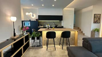 Una cucina moderna con isola centrale, sgabelli neri e un divano grigio in un ambiente soggiorno dalle linee contemporanee.