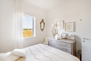 Ein Schlafzimmer mit Bett, Schminktisch, Fenster mit Blick auf ein Feld und Wandbildern.