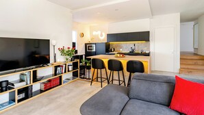 Una sala de estar moderna con un televisor de pantalla plana, una estantería y un sofá gris con un cojín rojo.