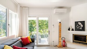 Una sala de estar moderna con un sofá gris, una chimenea y vistas al exterior con vegetación.