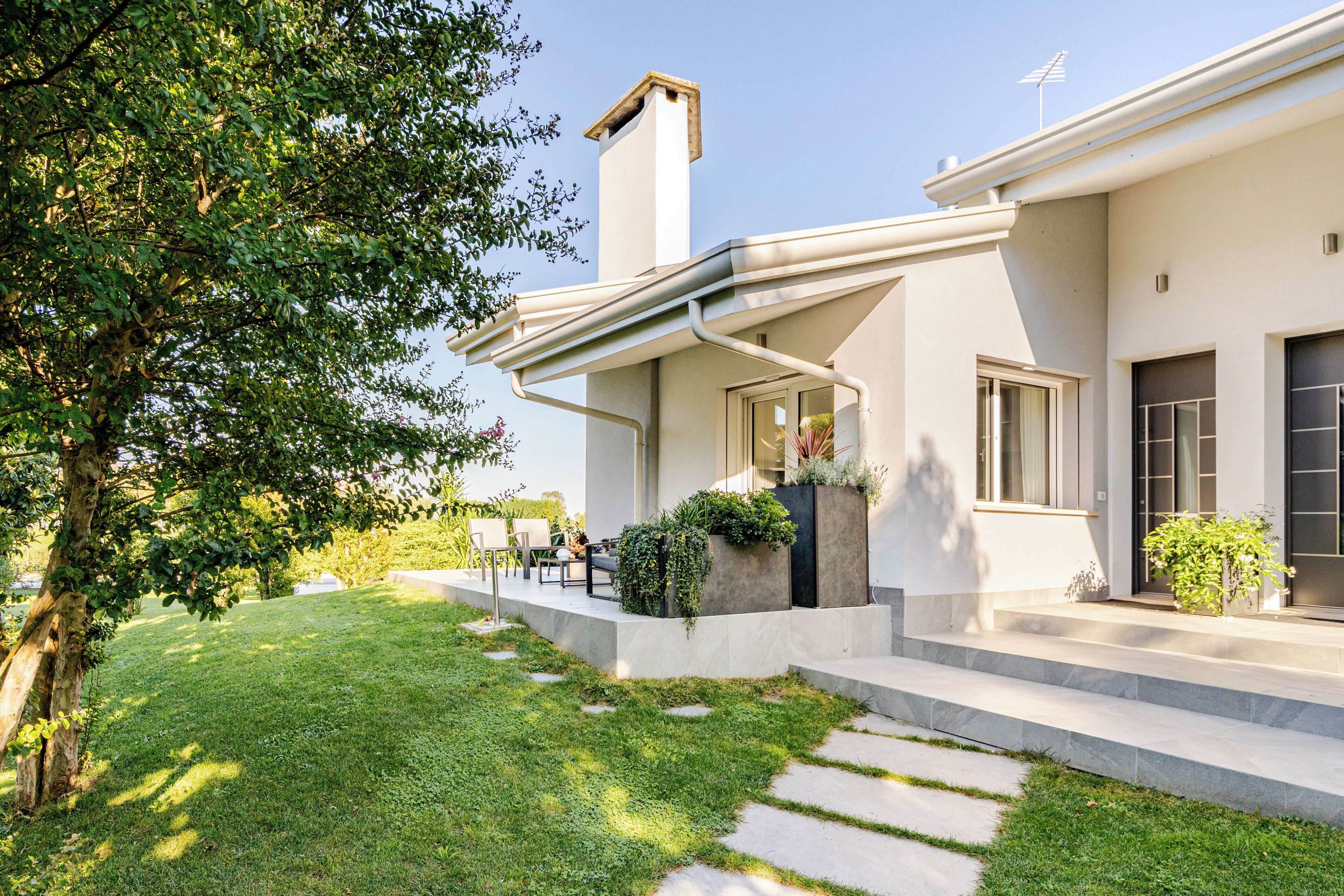 Una casa moderna con un portico coperto, un prato curato e un cielo sereno.