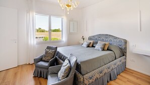 Un dormitorio con una cama grande, una silla, una araña y una ventana con vista a un campo.