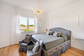 Ein Schlafzimmer mit einem großen Bett, einem Sessel, einer Chandelier und einem Fenster mit Blick auf ein Feld.