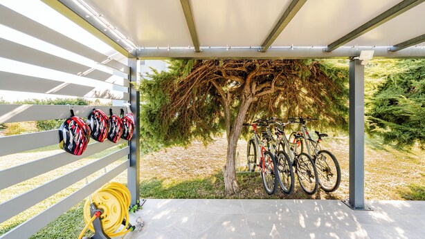 Un espacio de estacionamiento para bicicletas techado, con cascos y un carretel de manguera.