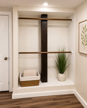 A room with a wooden floor, a white door, a shelf with a plant, and a basket.