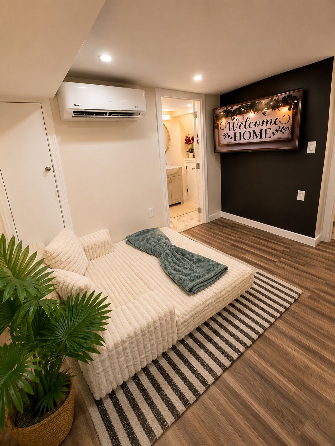 A bedroom with a bed, a potted plant, and a wall-mounted air conditioner.