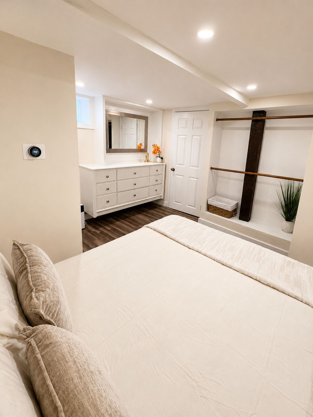 A bedroom with a bed, dresser, mirror, and a window with a plant.