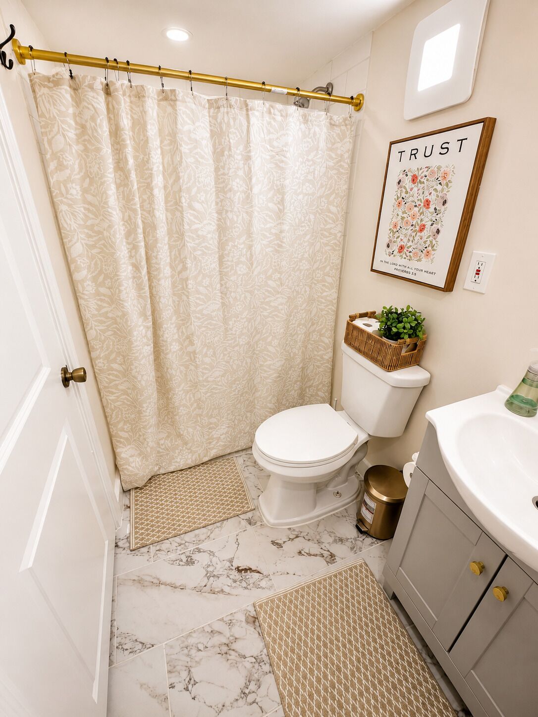 A bathroom with a toilet, a sink, a shower curtain, a framed quote on the wall, and a small plant on the sink.