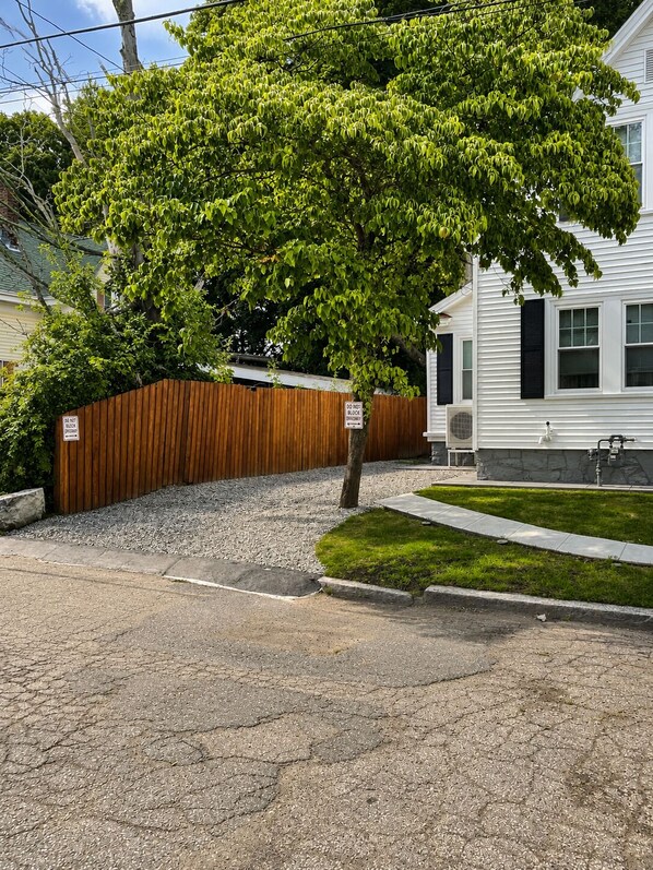 A residential street with a tree, a wooden fence, and a house with a white exterior.