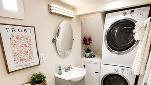 A bathroom with a toilet, sink, mirror, and two stacked washing machines.