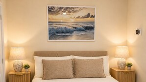 A bedroom with a large bed, two bedside tables with lamps, a globe, and a framed picture of a sunset over the ocean.