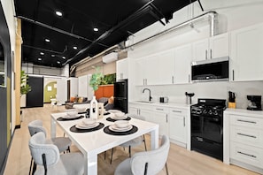A modern kitchen with white cabinets, a black stove, and a dining area with a table set for four. - Explore Petco Park & Gaslamp Nightlife - Sleeps 4! (San Diego)