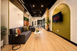 Ein modernes Interieur mit einem grauen Sofa, einem kleinen runden Tisch und einem an der Wand befestigten Fernseher mit dem Netflix-Logo.