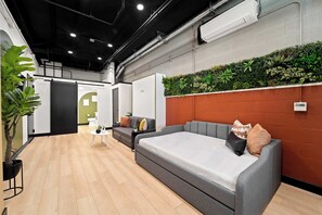 Ein modernes Interieur mit einem grauen Sofa, einem kleinen runden Tisch und einer grünen Wand mit Pflanzen.