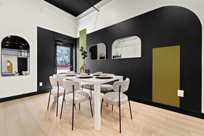 A modern dining area with a white table and grey chairs, a black and white wall with a mirror, and a window with a view of the outside. - Explore Petco Park & Gaslamp Nightlife - Sleeps 4! (San Diego)