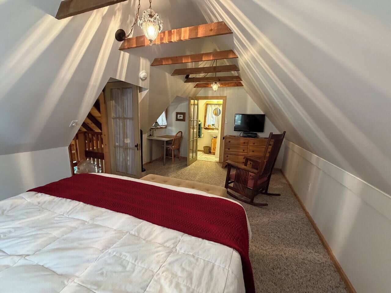 A bedroom with a bed, a desk, a chair, and a television in a loft-style room with sloped ceilings.