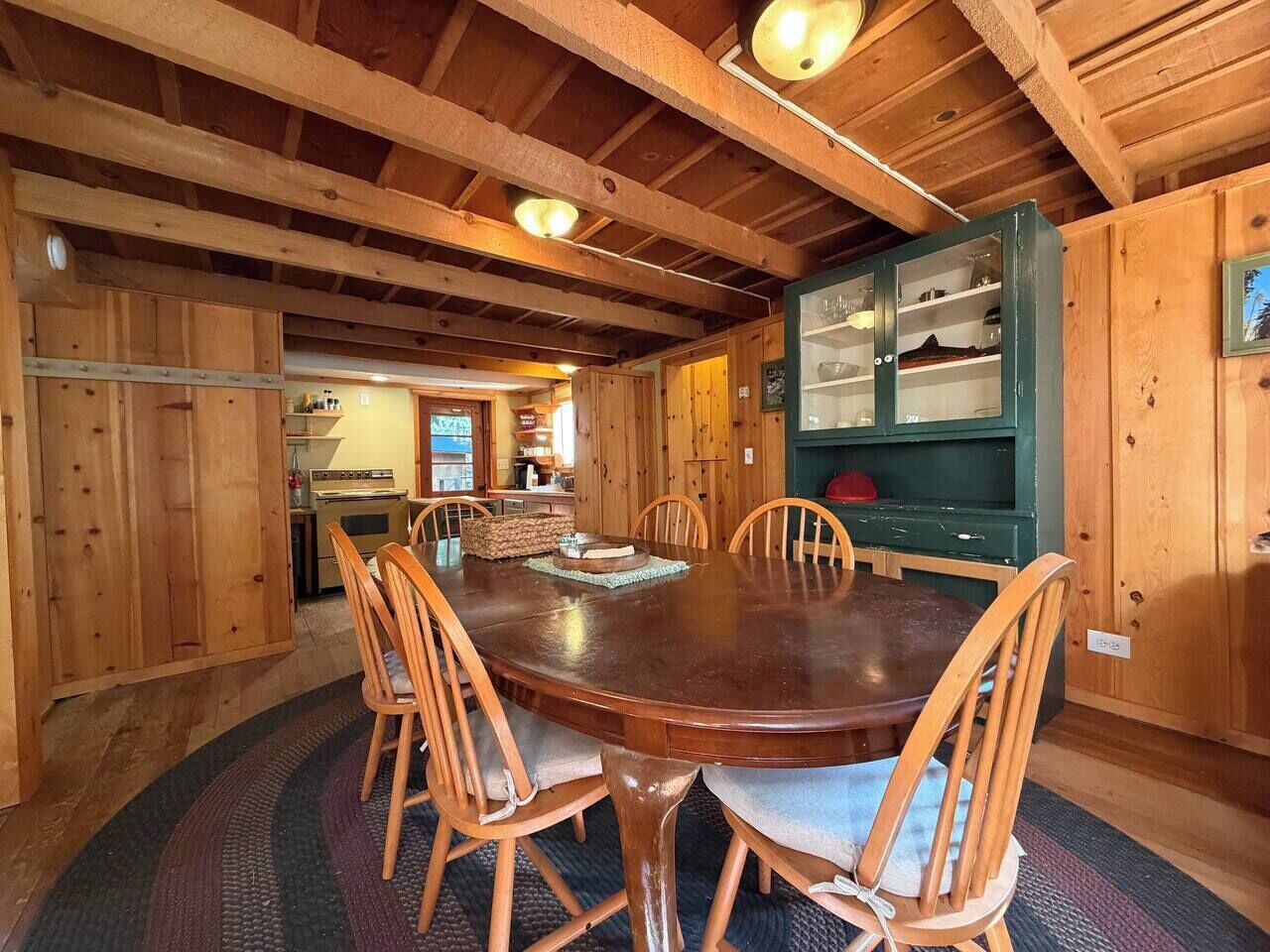 A wooden dining room with a round table and chairs, a kitchen in the background, and a green cabinet with glass doors.