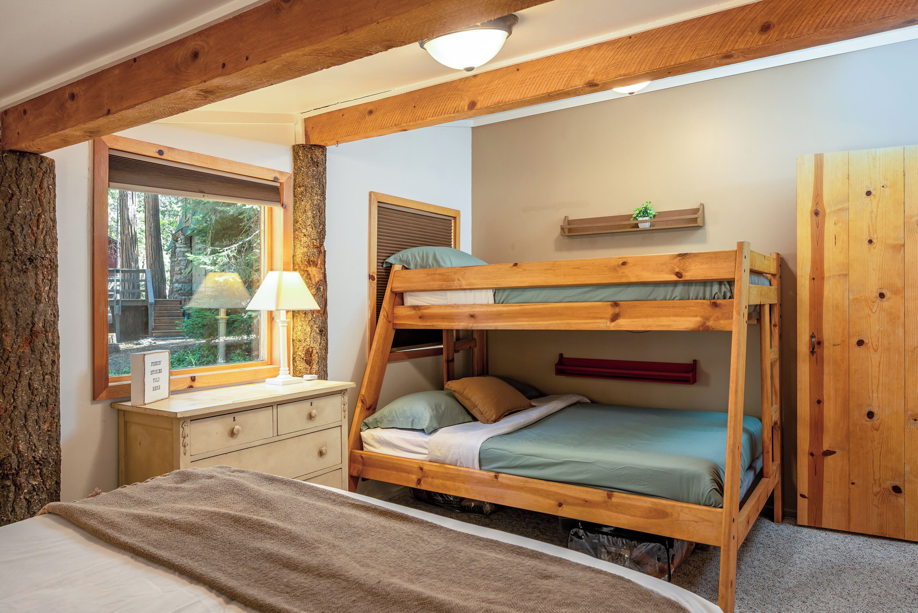 A bunk bed room with a desk, a lamp, and a window overlooking a natural landscape.