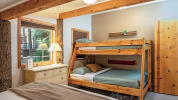 A bunk bed room with a desk, a lamp, and a window overlooking a natural landscape.