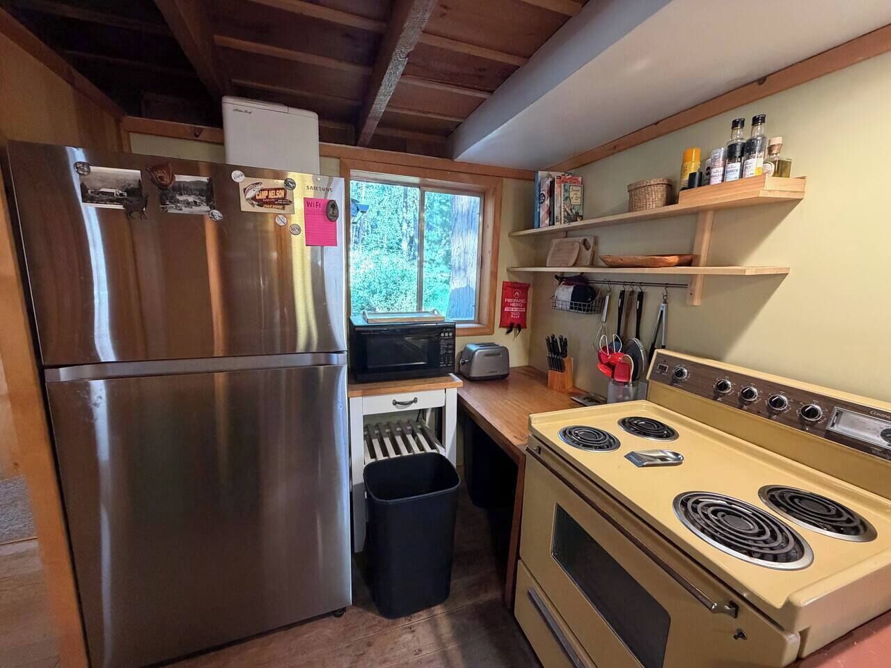 A compact kitchen with a stainless steel refrigerator, a microwave, a toaster, and a stove with four burners.