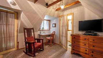 A cozy attic room with a sloped ceiling, a wooden rocking chair, a desk with a chair, a television, and a dresser.