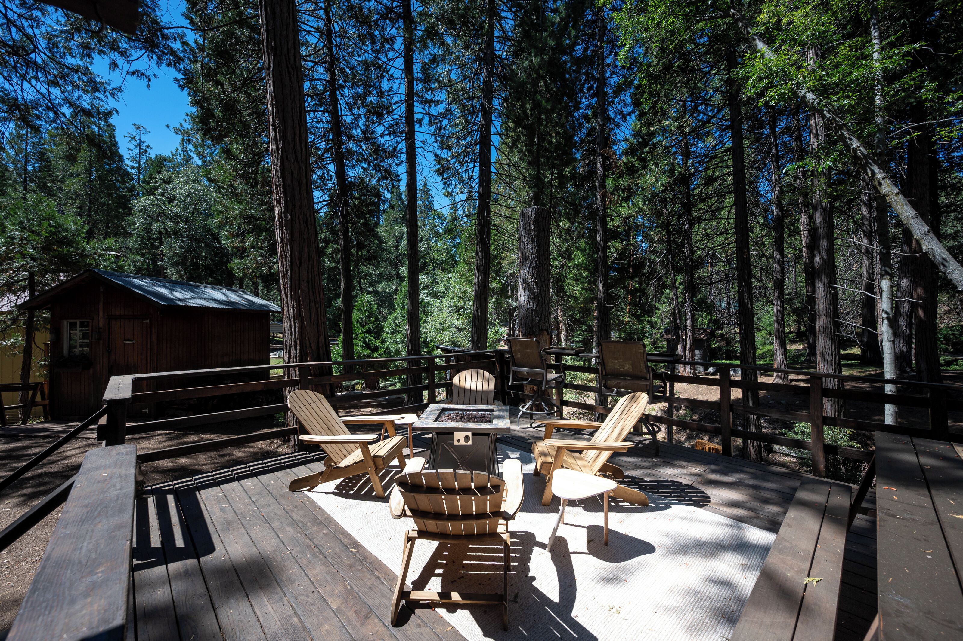 A wooden deck with outdoor seating, surrounded by tall trees.