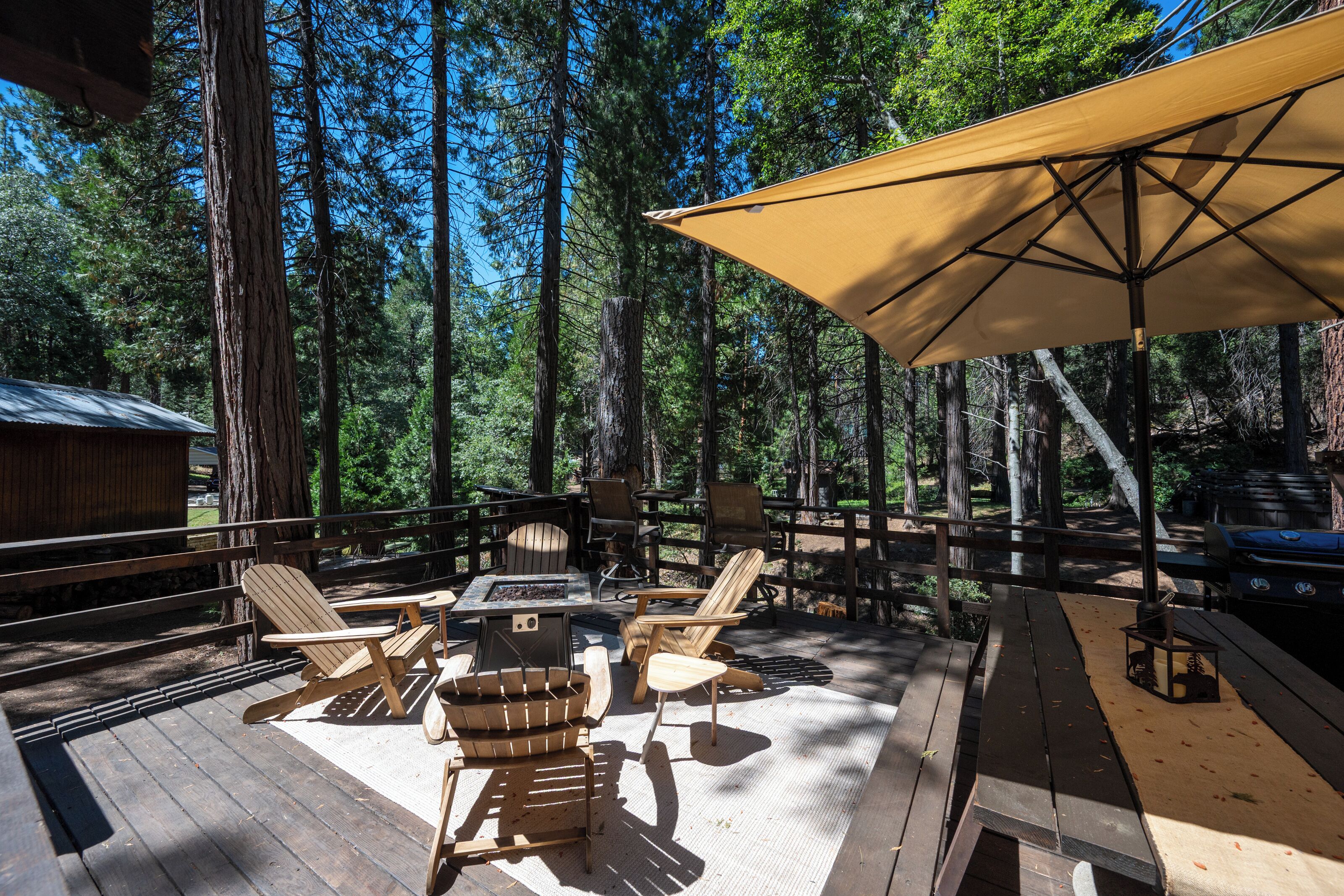 A wooden deck with outdoor furniture, including chairs and a table, surrounded by tall trees.