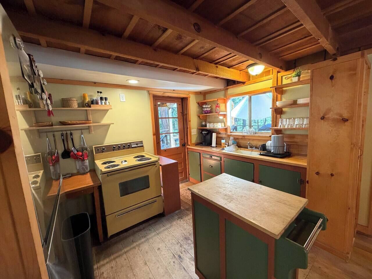 A compact kitchen with wooden cabinets, a stove, and a window overlooking a garden.