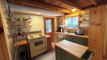 A compact kitchen with wooden cabinets, a stove, and a window overlooking a garden.